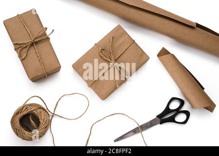 Gift wrapping process in recycled paper. Gift boxes, skein of twine, roll of brown paper and scissors on white background. DIY and zero waste concept Stock Photo