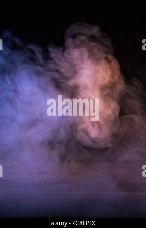Conceptual image of multi-colored smoke isolated on dark black background and wooden table. Stock Photo