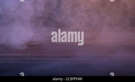Conceptual image of multi-colored smoke isolated on dark black background and wooden table. Stock Photo