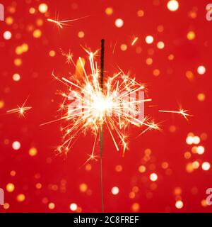 Christmas or Happy New Year concept. Close up of Brightly burning sparkler on a red background with lots of sparks. Stock Photo
