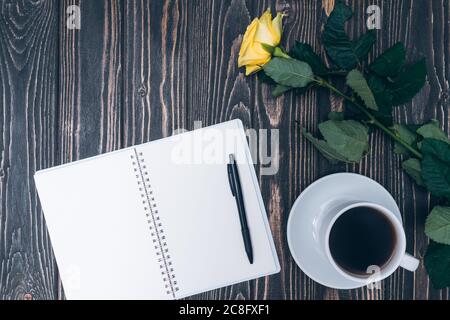 notebook, cup of coffee and yellow rose on wooden background. mock up Stock Photo
