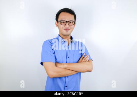 Portrait of a casually dressed young Asian man standing confidently with his arms crossed against a grey wall. Stock Photo