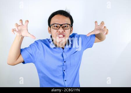 Young Asian Man wear blue shirt is funny angry face with shouting and pointing finger at camera isolated over white background Stock Photo