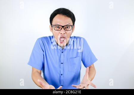 Young Asian Man wear blue shirt is funny angry face with shouting and pointing finger at camera isolated over white background Stock Photo