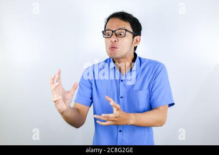 Young Asian Man wear blue shirt is funny angry face with shouting and pointing finger at camera isolated over white background Stock Photo