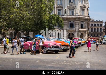 Havana / Cuba - 04.15.2015: Tourists and local people walking in front of colorful classic american cars which are used as touristic taxis in Cuba Stock Photo