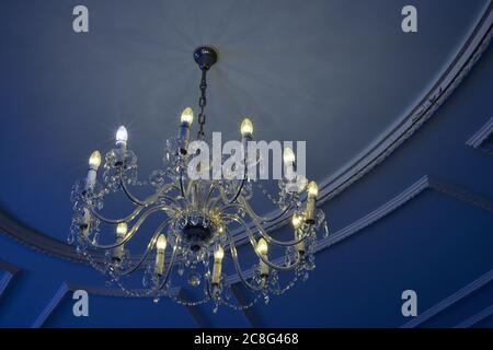 Comparison of energy saving vs regular bulbs in a glass chandelier under a blue ceiling. Stock Photo