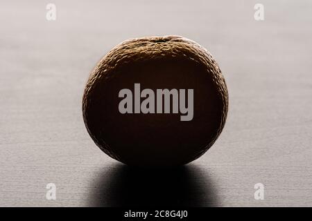 A mandarin orange (Citrus reticulata) on a table. Backlit against a white background. Stock Photo