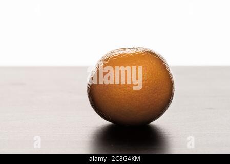 A mandarin orange (Citrus reticulata) on a table. Backlit against a white background. Stock Photo