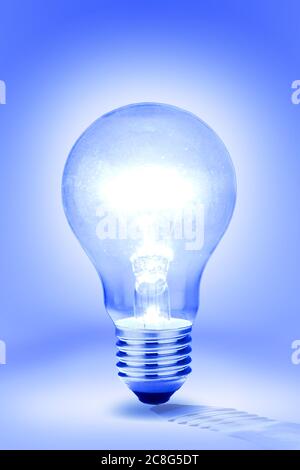 lit incandescent light bulb against blue background Stock Photo
