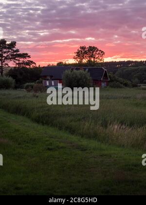 Sonnenuntergang Sonnenaufgang auf einem Getreidefeld auf der Insel Rügen mit einer Farm, Bäumen, Strohballen, roten Mohnblumen nach einem Gewitter Stock Photo