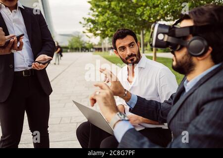 Mixed race group of businessmen hanging out together in town, wearing VR headsets. Stock Photo