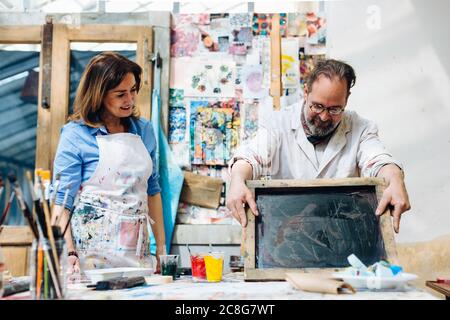 Woman watching man do silk screen print in creative studio Stock Photo