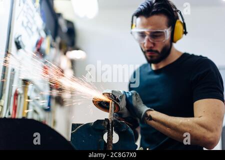 Young man using angle grinder on metal in workshop Stock Photo