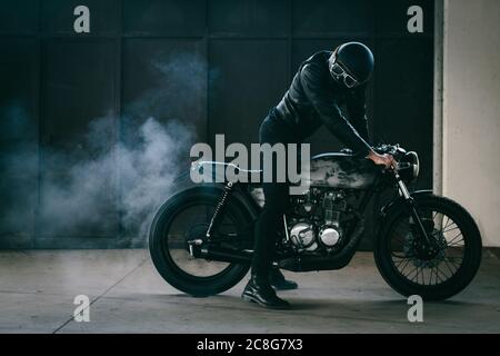 Young male motorcyclist revving vintage motorcycle in garage Stock Photo