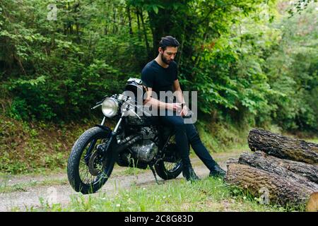 Young male motorcyclist on vintage motorcycle on rural roadside looking at smartphone, Florence, Tuscany, Italy Stock Photo