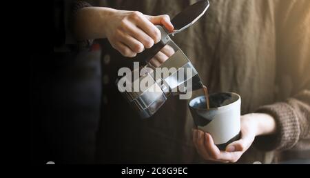 Barista pouring coffee from moka pot coffee maker to the small coffee cup . Professional coffee brewing. Stock Photo