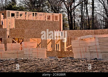 Wood frame building under construction with roof trusses piled in front Stock Photo