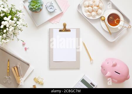 Flat lay desk table. Workspace with modern notebook, stationery, succulent, jewelry and a cup of tea on white table. Top view. Feminine concept Stock Photo