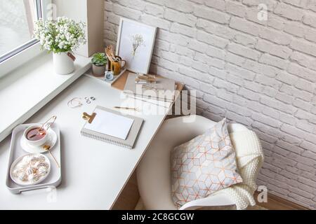 Work table near the window in the Scandinavian Nordic style. Female work and home office concept. White and gold office. Flowers in a vase and rings Stock Photo