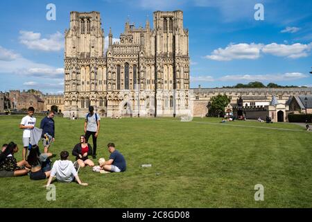 Young people on the grass with the West Front of Wells Cathedral and Cathedral Green, Wells, Somerset, England behind Stock Photo