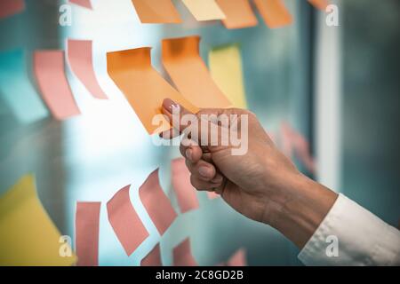 Female hand glues empty sticker on office window. Many colorful note paper stickers with space for text pasted on glass wall. Tinted image Stock Photo