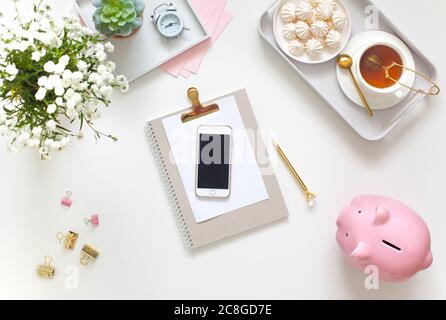 Flat lay desk table. Workspace with modern notebook, stationery, succulent, jewelry and a cup of tea on white table. Top view. Feminine concept Stock Photo