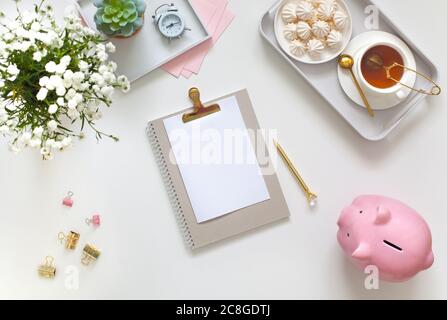 Flat lay desk table. Workspace with modern notebook, stationery, succulent, jewelry and a cup of tea on white table. Top view. Feminine concept Stock Photo