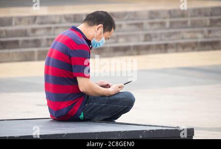 Asian man wearing face man covering looking at mobile phone. Stock Photo
