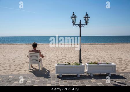Tourist sitting in a chair on a lonely sandy beach, Black Sea, Zatoka, Odessa, Ukraine Stock Photo