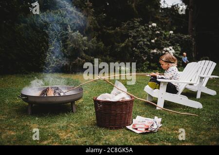 White child holding stick sitting on chair making smores in bonfire Stock Photo