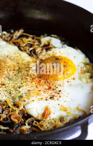 Fried eggs with onions and spices in a cast iron skillet. Stock Photo