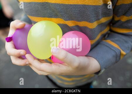 Child wearing striped shirt carefully holds water balloons in hands Stock Photo