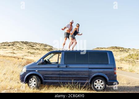 happy couple surfing on top of the van. Stock Photo