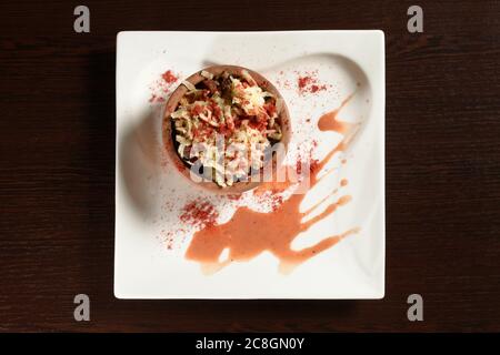 Baked beef meat in a clay pot with cheese and paprika on a square plate on a wooden table, top view Stock Photo