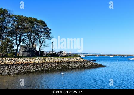 Plymouth, MA harbor with stone wall, dock and reproduction colonial house with stone jetty in background Stock Photo