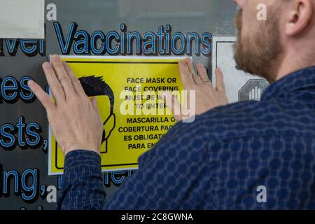 London, UK. 24th July, 2020. A man puts up a notice out side a doctors surgery in South London telling people face masks must be worn before entering.The Government has made it mandatory to wear face coverings on all public transport and in shops in England. Credit: SOPA Images Limited/Alamy Live News Stock Photo