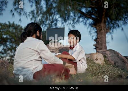 Two happy elementary students with a book and computer studying at natural park, New Normal Education concept Stock Photo