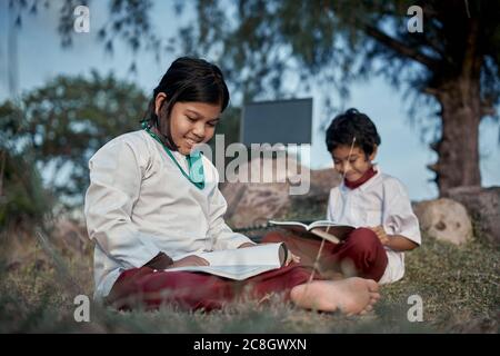 Two happy elementary students with a book and computer studying at natural park, New Normal Education concept Stock Photo