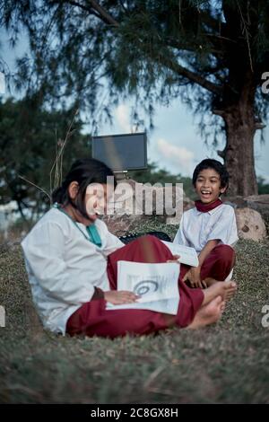 Two happy elementary students with a book and computer studying at natural park, New Normal Education concept Stock Photo