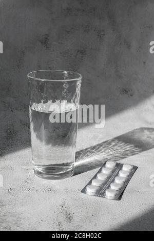 Transparent glass of water with white pills in contrast light. Headache concept Stock Photo