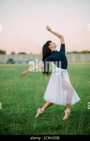 Japanese ballerina in white skirt dances on lawn background. Stock Photo