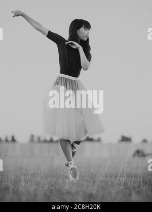 Japanese ballerina in white skirt dances on lawn background. Black and white image. Stock Photo