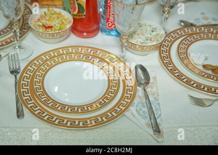 Empty plate , gold set on wooden white table . Beautifully decorated table with gold plates, linen napkin , spoon, fork . Stock Photo