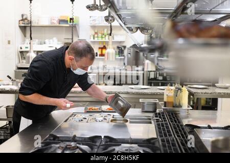 Chef in uniform cooking in a commercial kitchen. Male cook wearing apron standing by kitchen counter preparing food. High quality photo Stock Photo