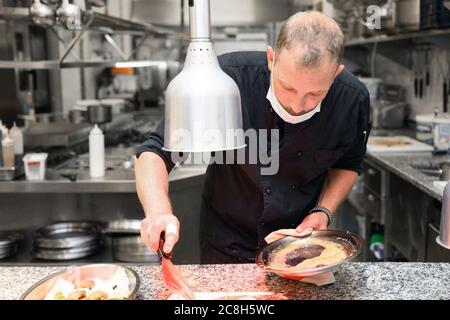 Chef in uniform cooking in a commercial kitchen. Male cook standing by kitchen counter preparing food. High quality photo
