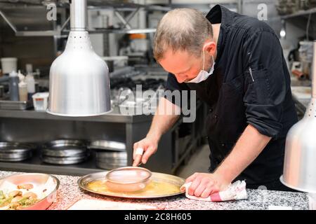 Chef in uniform cooking in a commercial kitchen. Male cook standing by kitchen counter preparing food. High quality photo Stock Photo