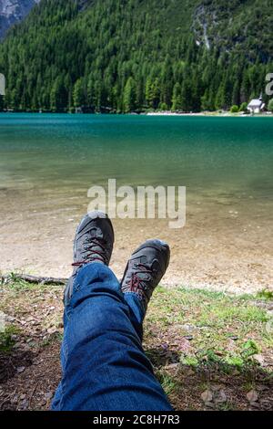 Trekking legs of a man lying on the shore of a lake enjoying the mountain landscape Stock Photo