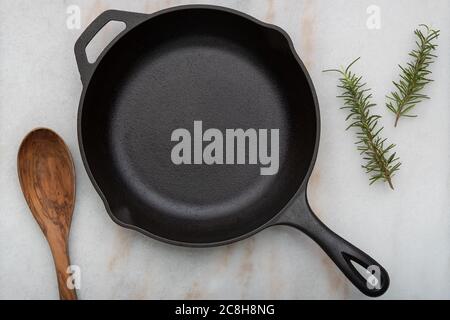 Cast Iron frying pan with spoon on white background with Rosemary Sprigs Stock Photo