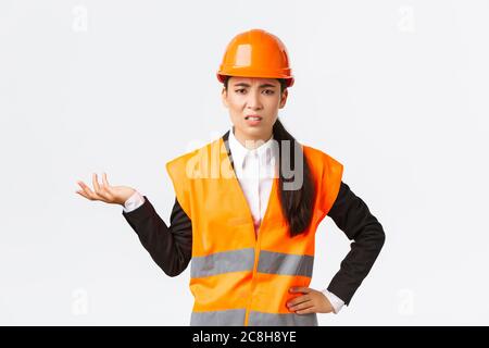 So what, wtf going on. Frustrated and disappointed asian female chief engineer complaining on employees, scolding someone, wear reflective jacket and Stock Photo